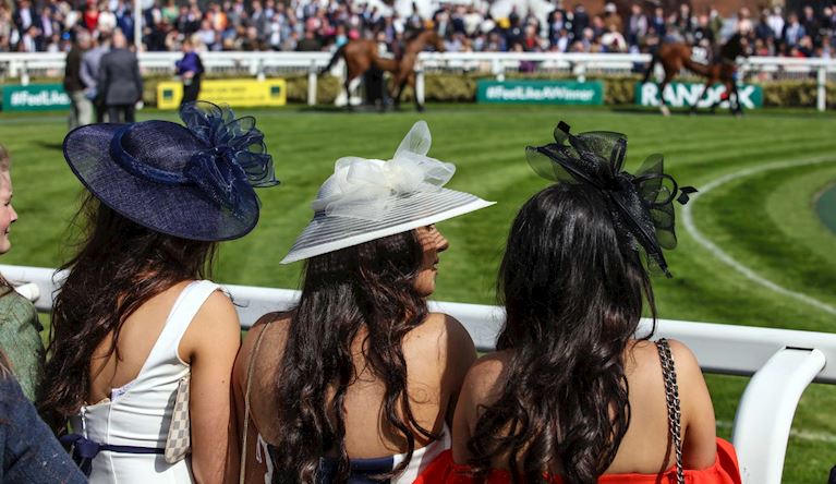 Three women in big hats looking down over the parade ring on a sunny day