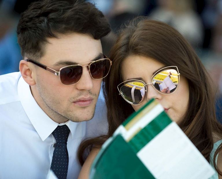 A young couple wearing sunglasses reading the grand national racecard