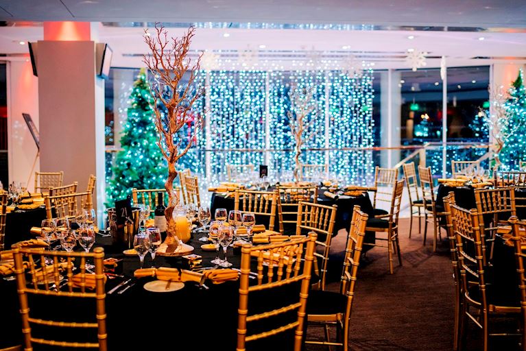 Round tables set up with black table cloths and gold chairs for Christmas parties